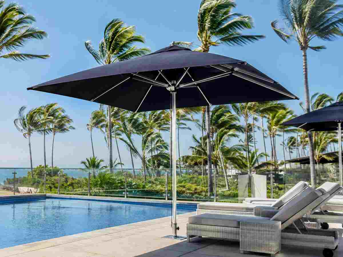 Ausbrella-style wind-rated umbrella standing firm beside a resort pool as palm trees sway in coastal wind